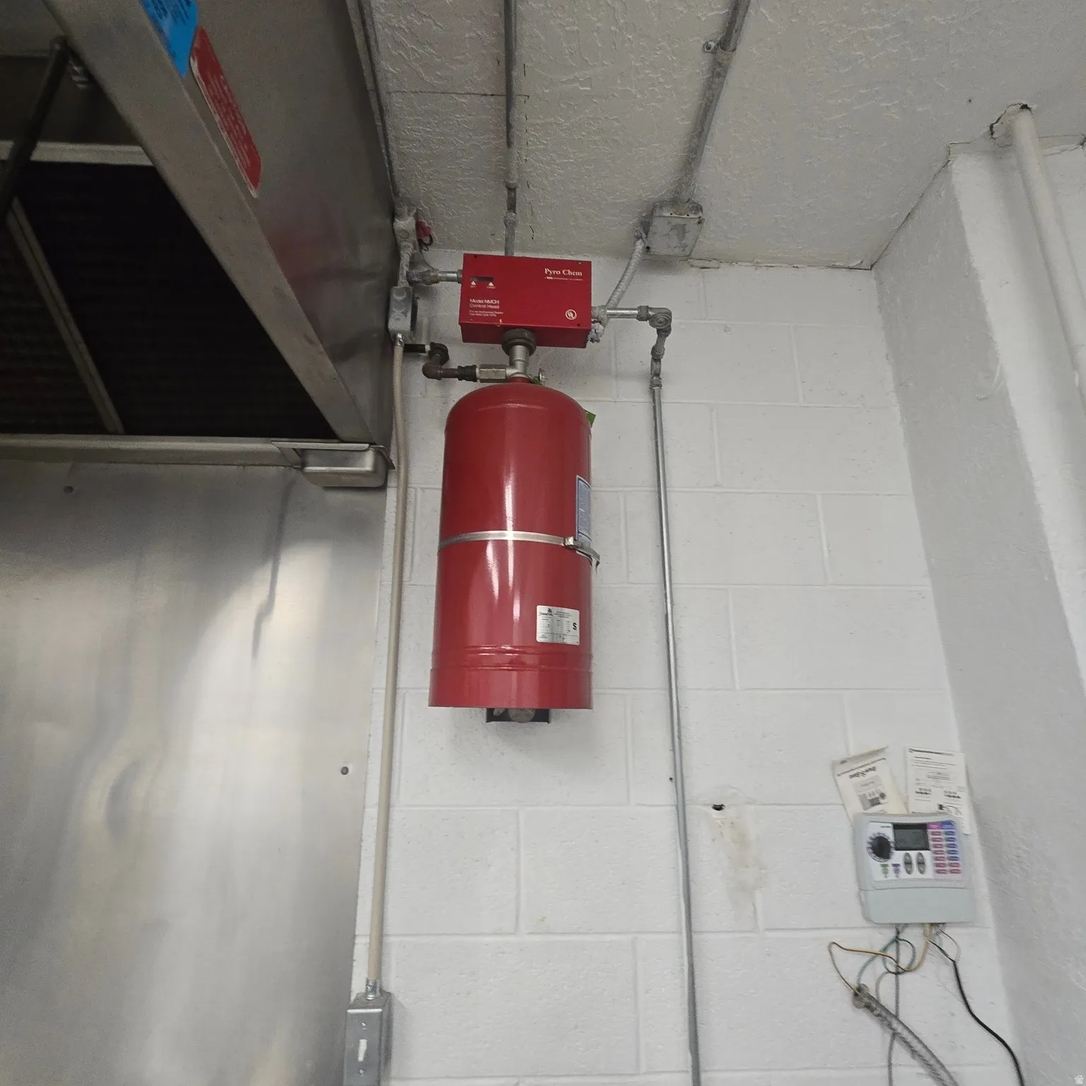 Commercial-grade stainless steel exhaust hood and a wall-mounted fire suppression system with a red cylinder and control panel