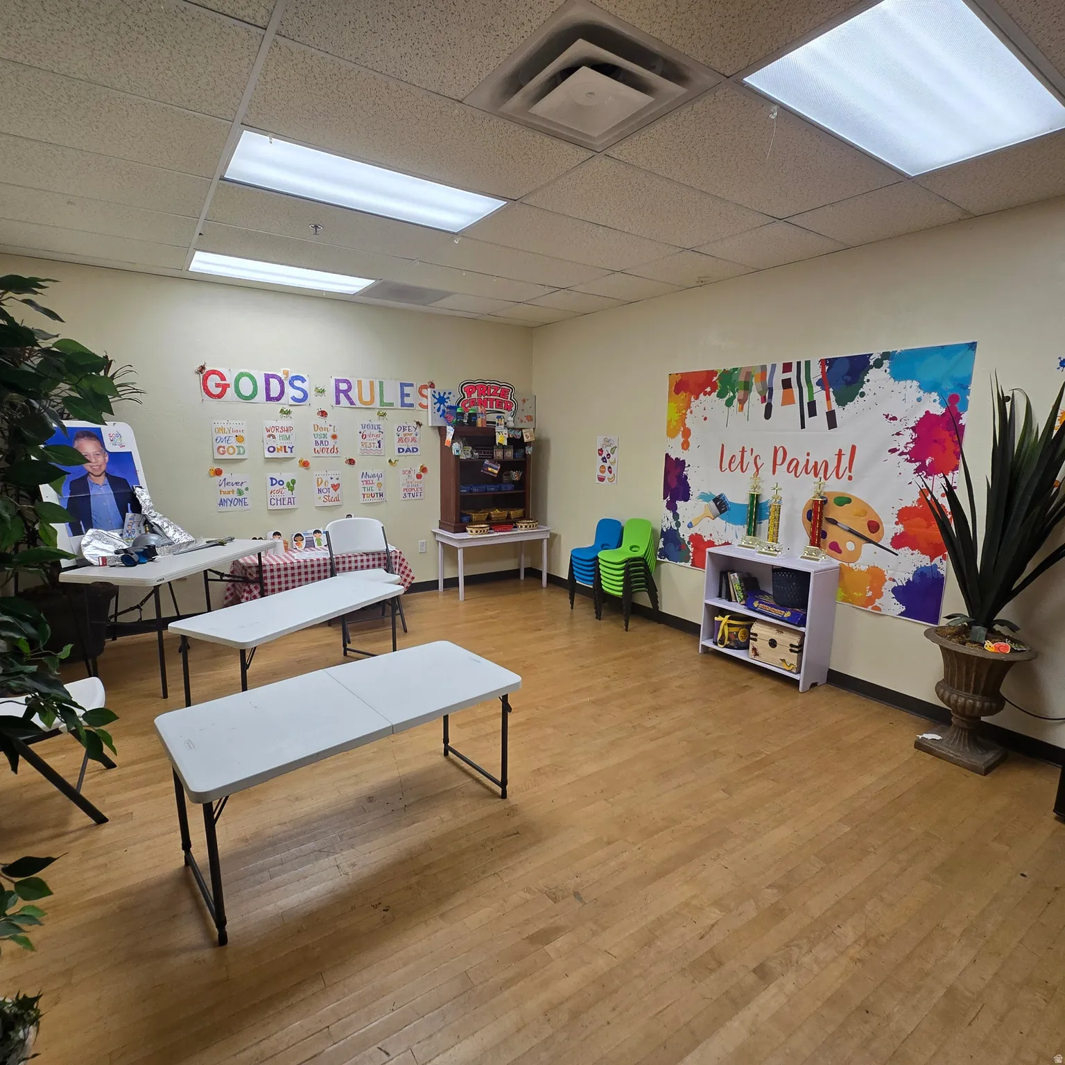 Spacious room featuring wood-finish flooring, drop ceiling with integrated fluorescent lighting, and light-toned walls