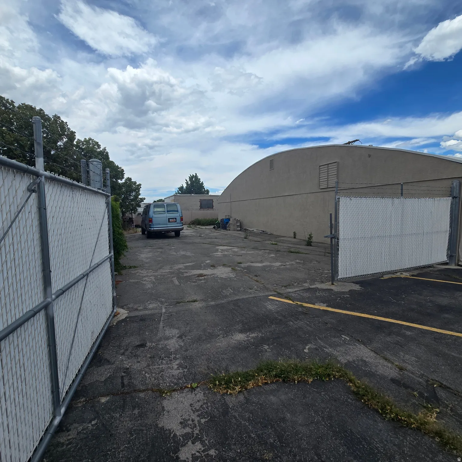 Paved lot with chain-link fencing and gate, featuring a large structure with a curved roofline