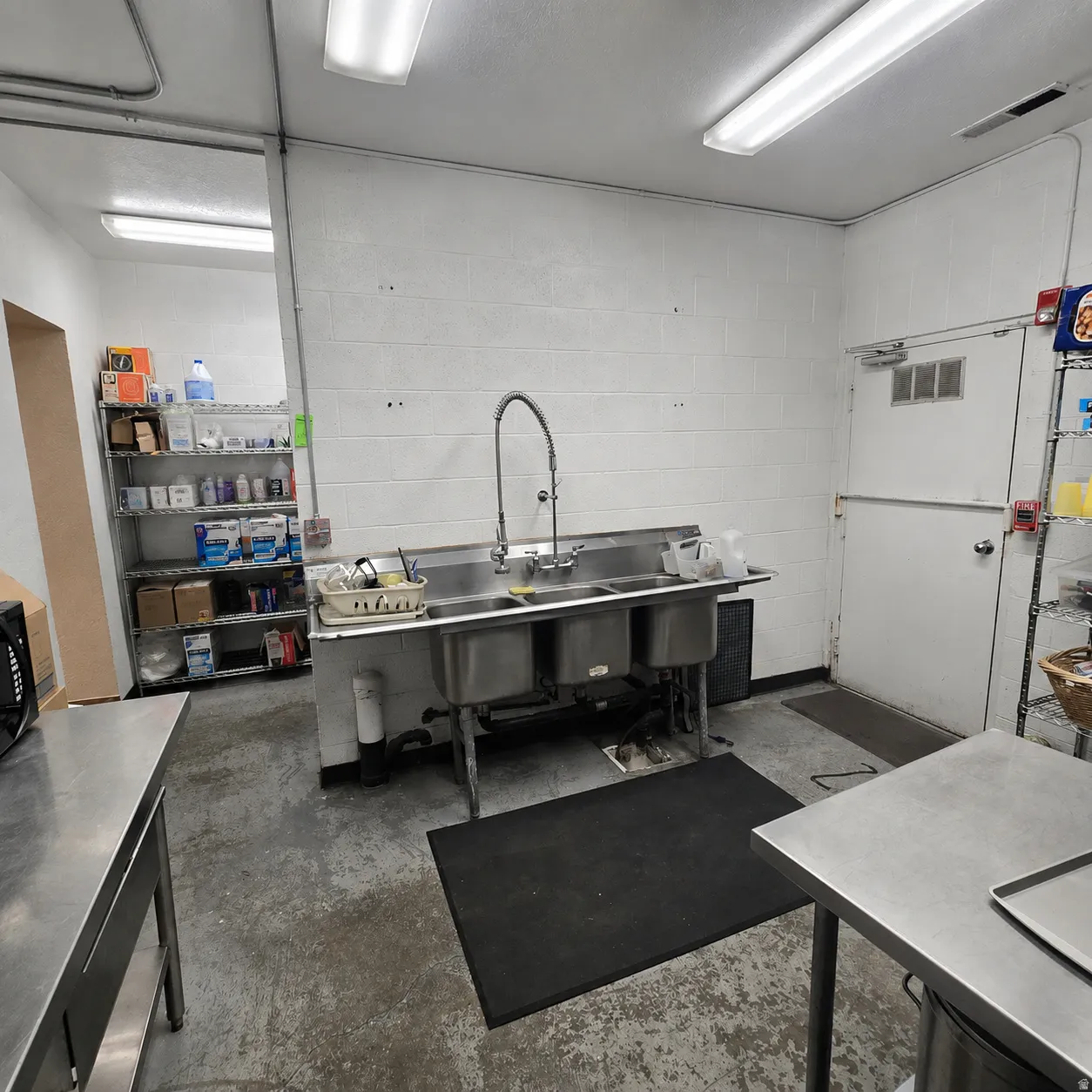Industrial-style utility room featuring a triple basin stainless steel sink with a gooseneck faucet, concrete flooring, and white painted block walls