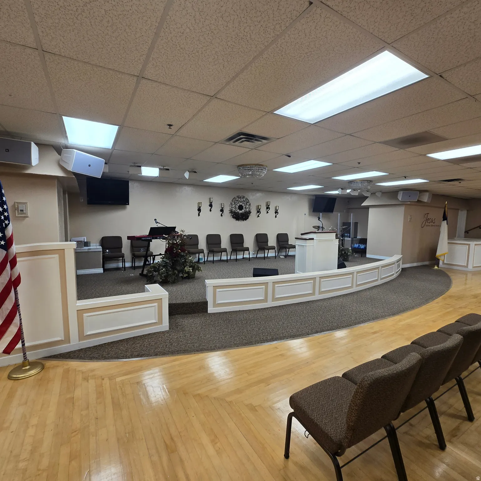 Spacious assembly room featuring a raised platform with white paneling and a carpeted stage area