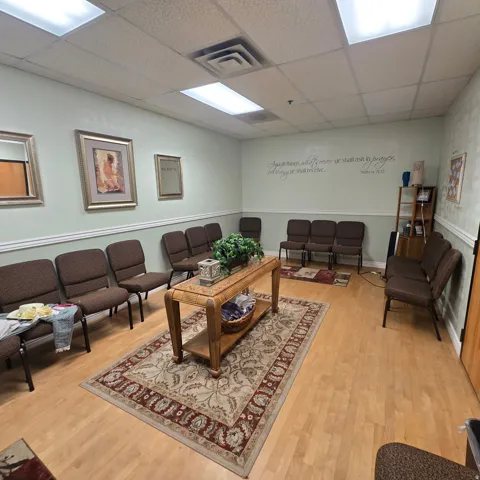 Spacious waiting area featuring light wood-finish flooring, a drop ceiling with recessed lighting, and pale green walls with white chair rail molding