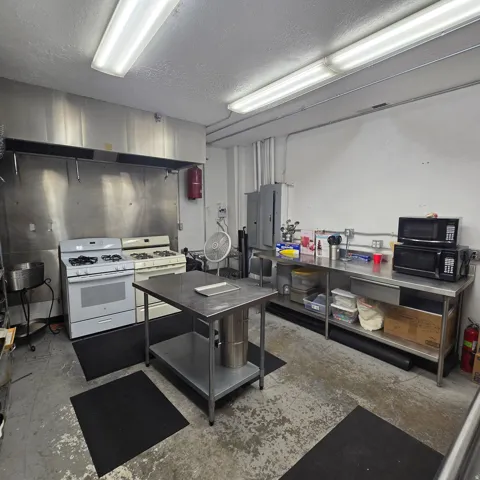 Commercial kitchen space featuring two gas ranges with a stainless steel vent hood, extensive stainless steel countertops, and a central stainless steel prep table