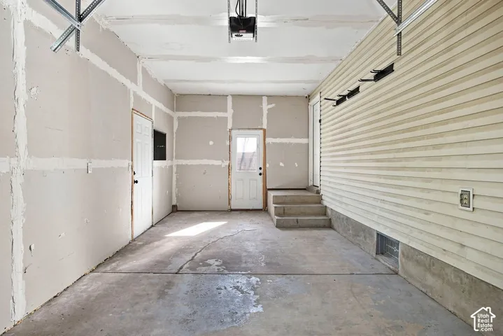 Spacious concrete floor garage with two entry doors, concrete steps, and exposed wall framing