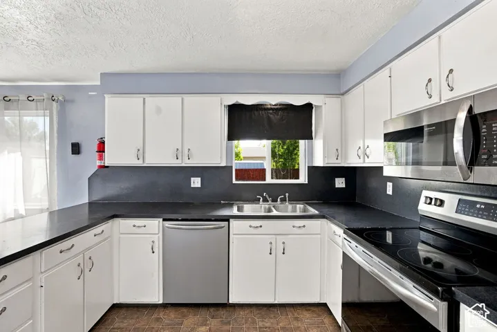 White cabinetry with dark countertops, stainless steel appliances, and a double basin sink