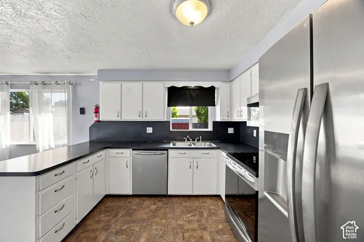 Kitchen featuring white cabinetry, dark countertops, stainless steel appliances, and wood-finish flooring
