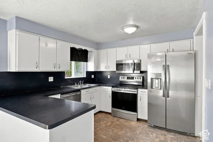 U-shaped kitchen featuring white cabinetry, dark countertops, a stainless steel side-by-side refrigerator, stainless steel range, and a stainless steel microwave