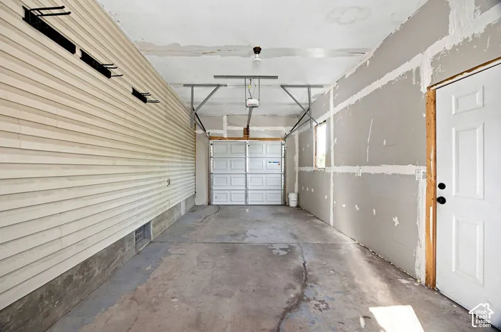 Concrete flooring, paneled garage door, exposed drywall, single light fixture, single panel door