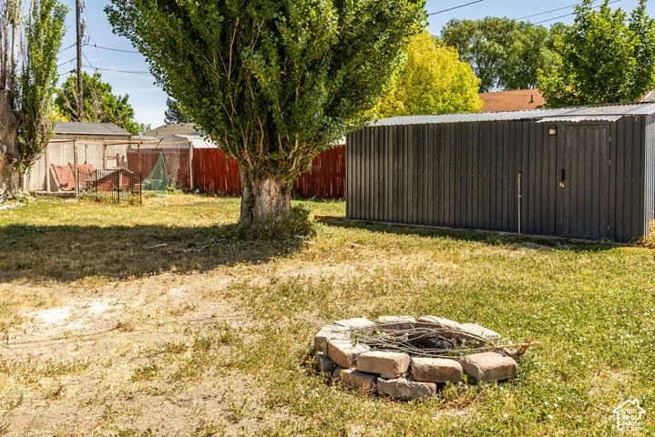 Spacious backyard featuring a stone fire pit, mature tree, and a corrugated metal shed with a side door