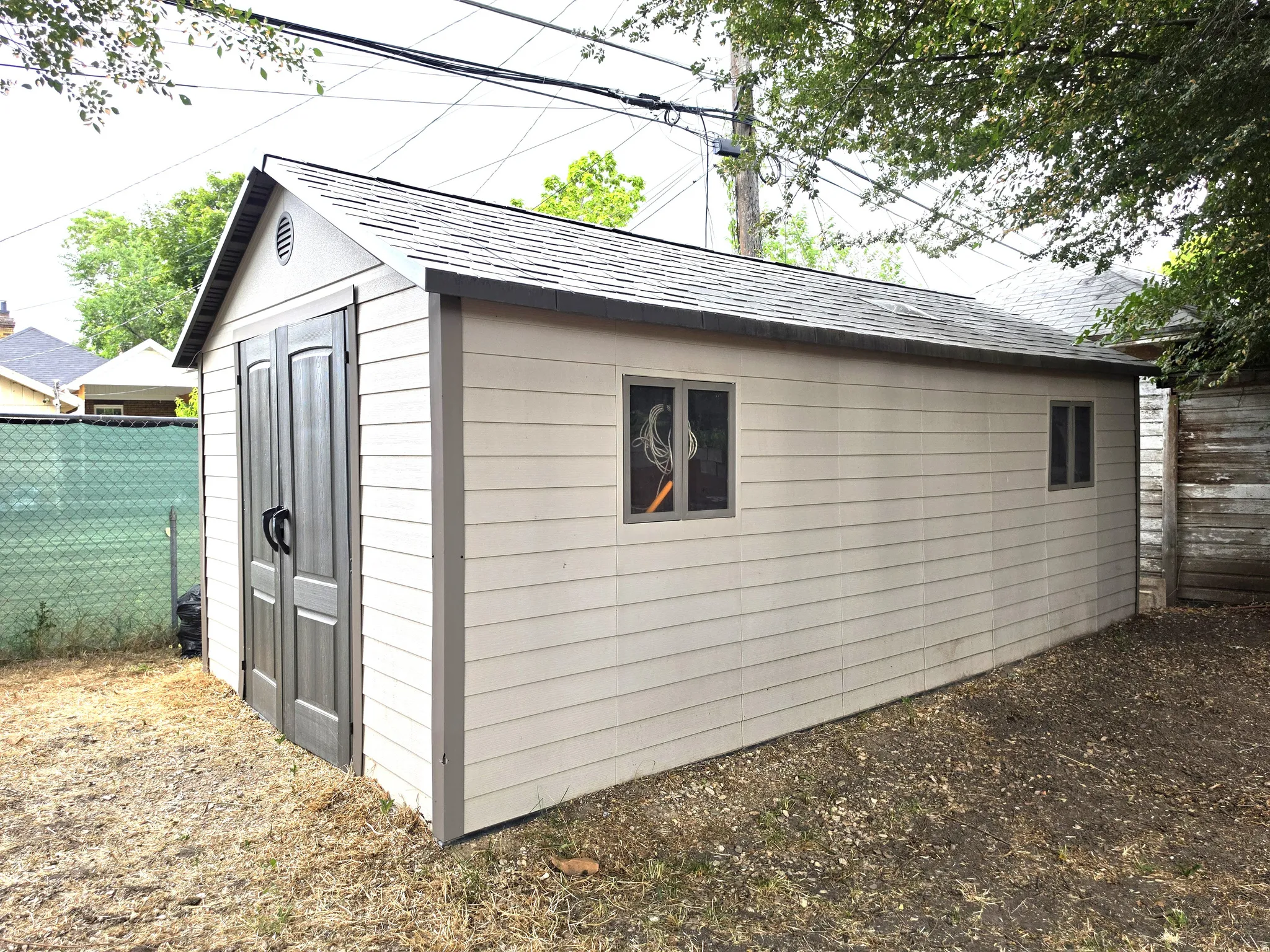 Detached storage shed with dual front entry doors, shingle roof, two windows, and horizontal siding