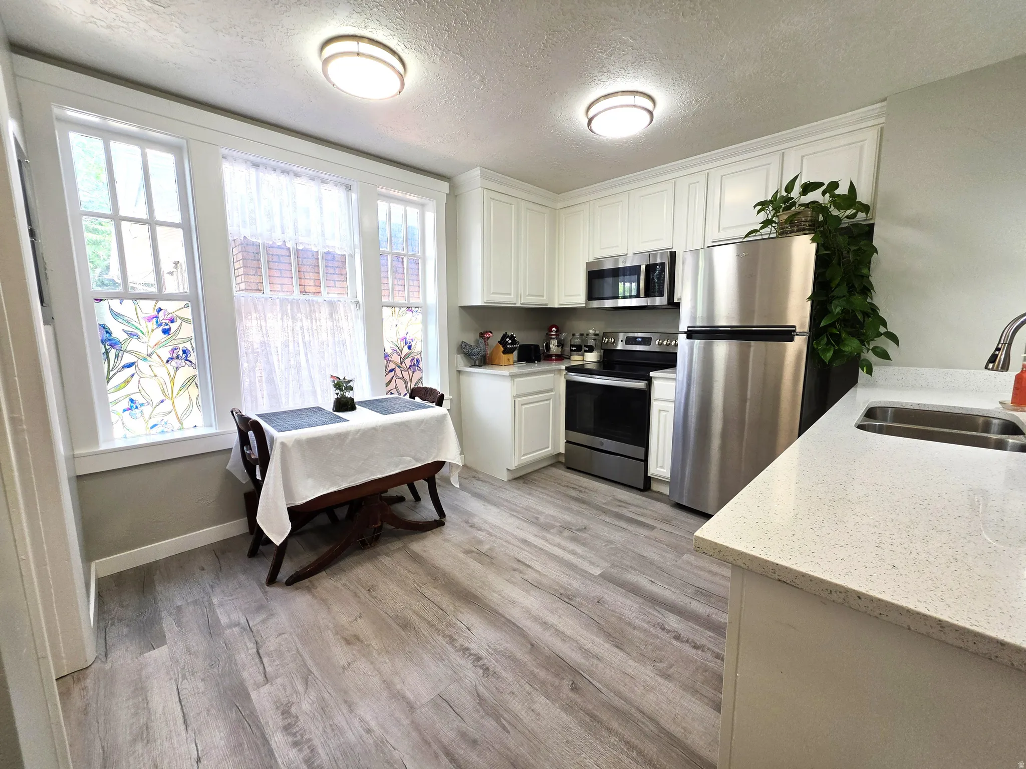 Kitchen featuring white cabinetry with crown molding, stainless steel appliances, a double basin sink, light-toned countertops, and wood-finish flooring