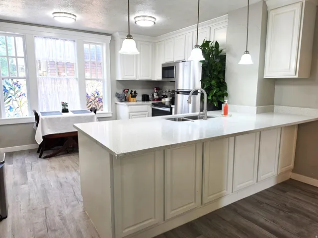 Kitchen with white cabinetry, light-colored countertops, stainless steel appliances, and wood-finish flooring
