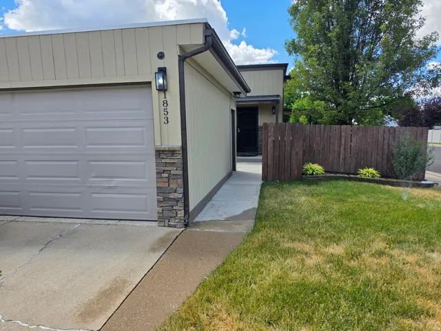 Exterior featuring a light tan facade, attached garage, stone accents, and a dark brown privacy fence