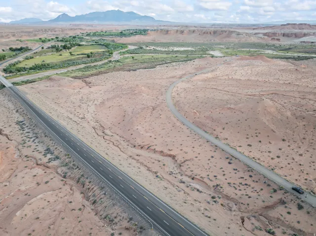 Expansive desert landscape featuring a paved highway, unpaved road, and distant green riverbed