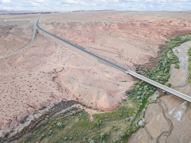 Aerial perspective showcasing a bridge spanning a riverbed with verdant vegetation, surrounded by arid, expansive terrain