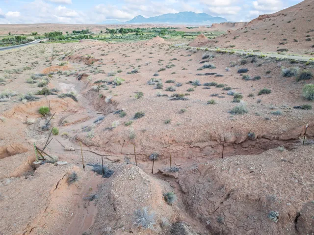 Arid landscape featuring a natural wash, distant green vegetation, and mountain backdrop