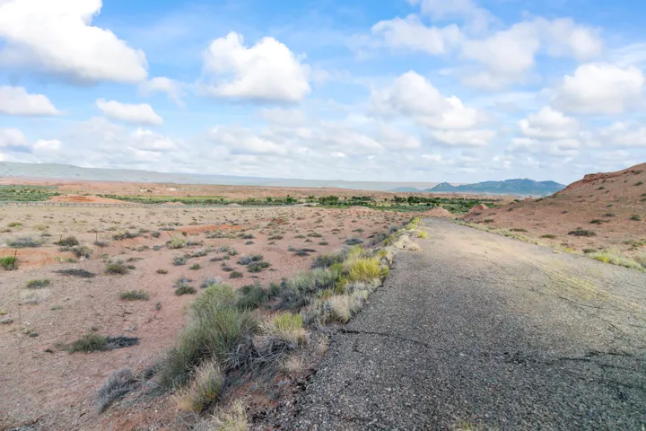 Expansive undeveloped land featuring a paved road, scattered low-lying vegetation, and distant natural terrain