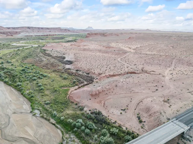 Expansive desert landscape featuring a riverbed, arid terrain, distant mesas, and a paved road