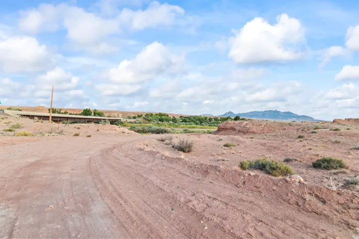 Expansive desert landscape featuring a dirt road, distant green vegetation, and rugged terrain