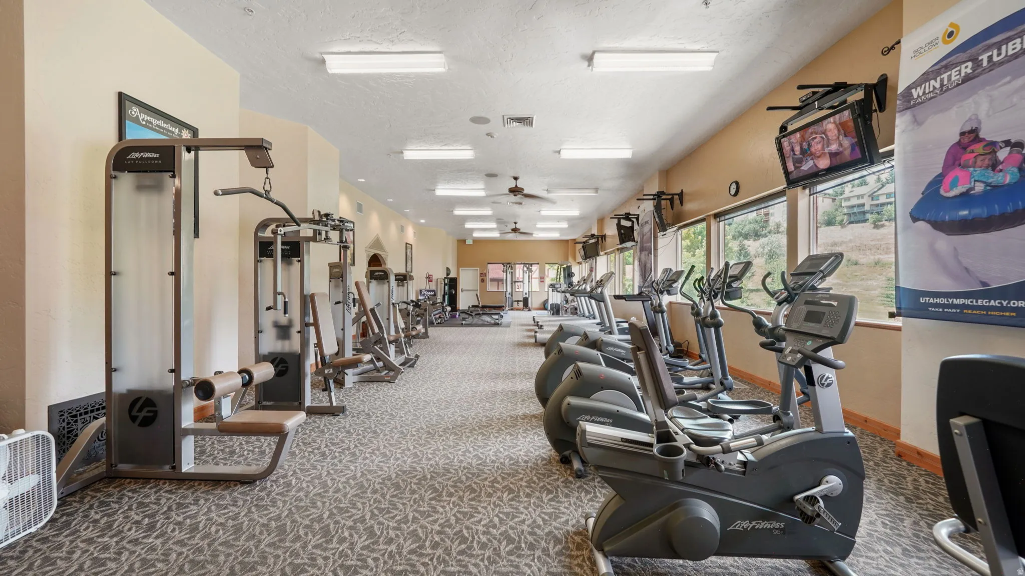 Dedicated fitness area featuring multiple exercise machines, patterned carpet flooring, and recessed lighting