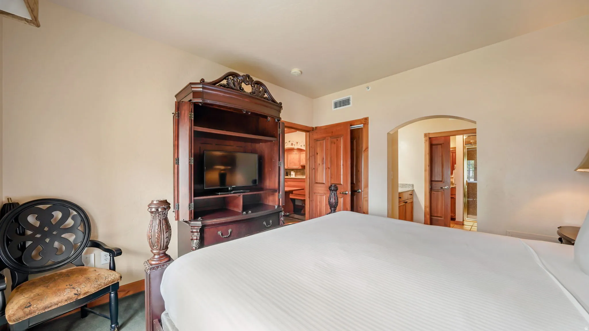 Primary bedroom featuring light-toned walls, wood-finish flooring, an entertainment armoire, a decorative archway to bathroom, and wood panel doors