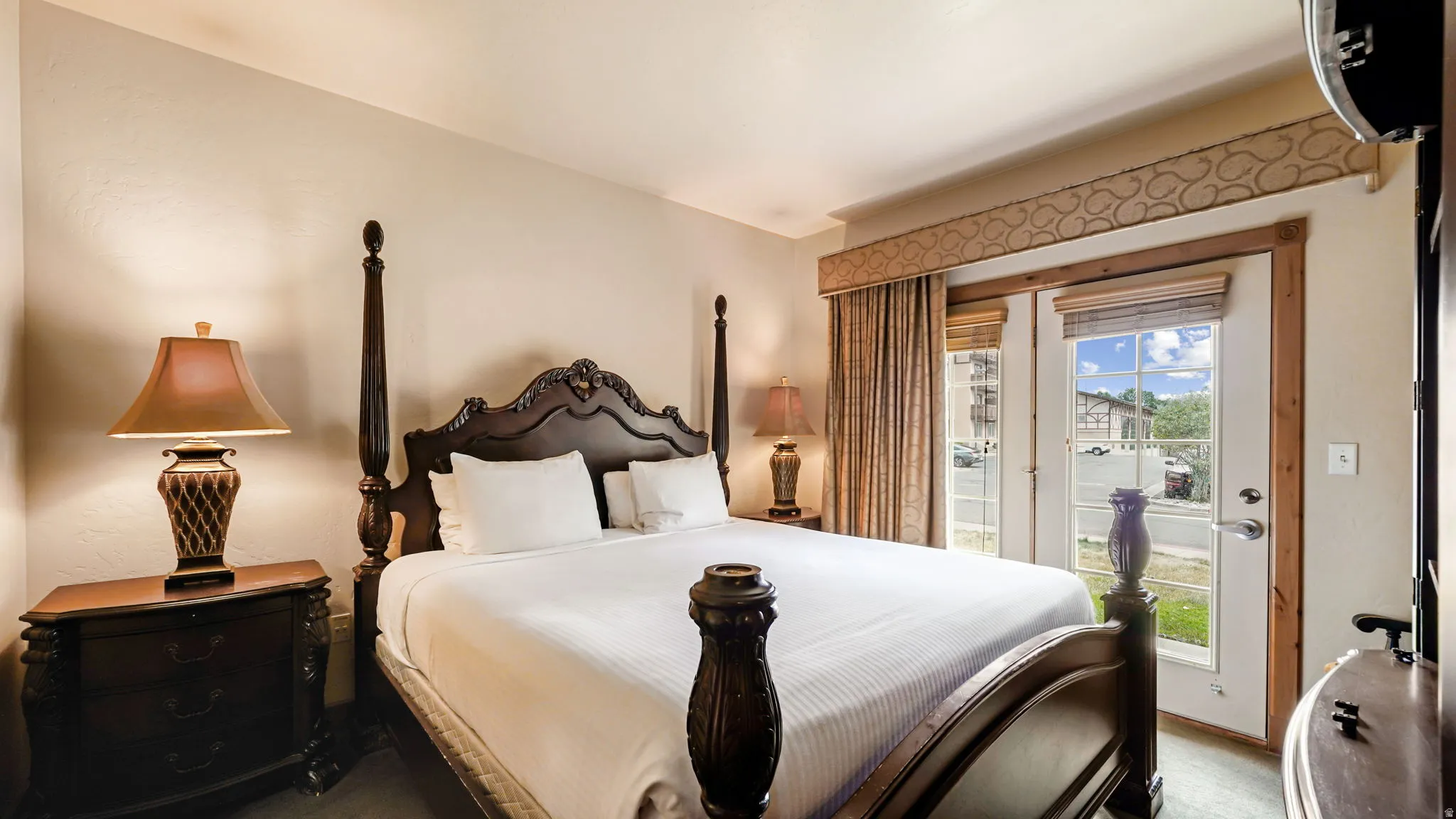 Primary bedroom with main level french doors to small private patio, carved wood-finish bed frame, nightstand, and dresser