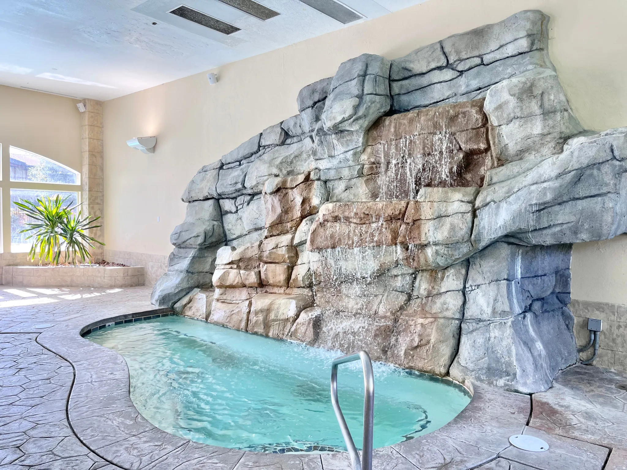 Indoor spa featuring a rock waterfall, stamped concrete flooring, and an integrated planter with natural light from large windows