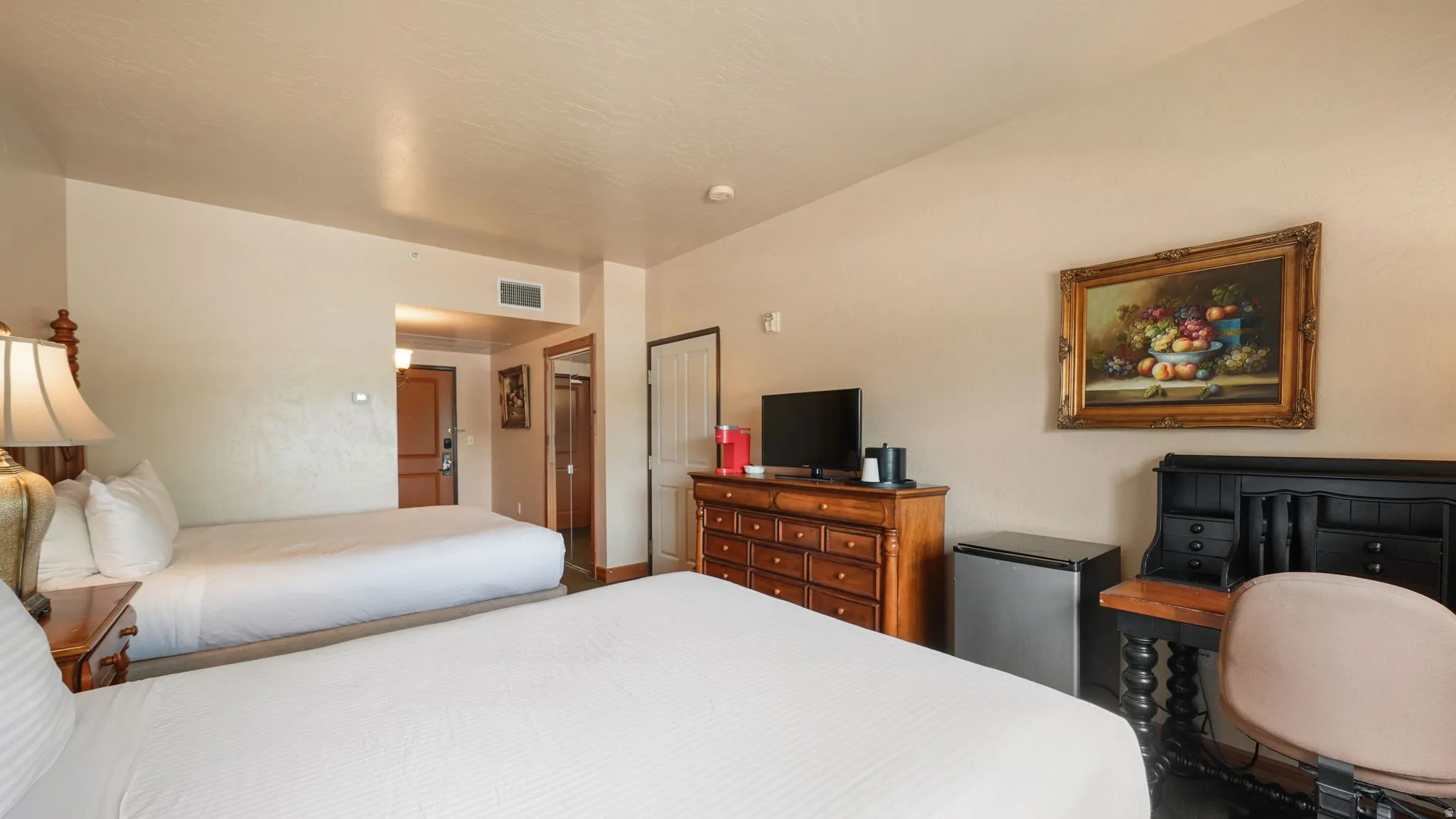 Spacious 2nd bedroom featuring two large beds, a wood-finish dresser with television, and a built-in mini-refrigerator