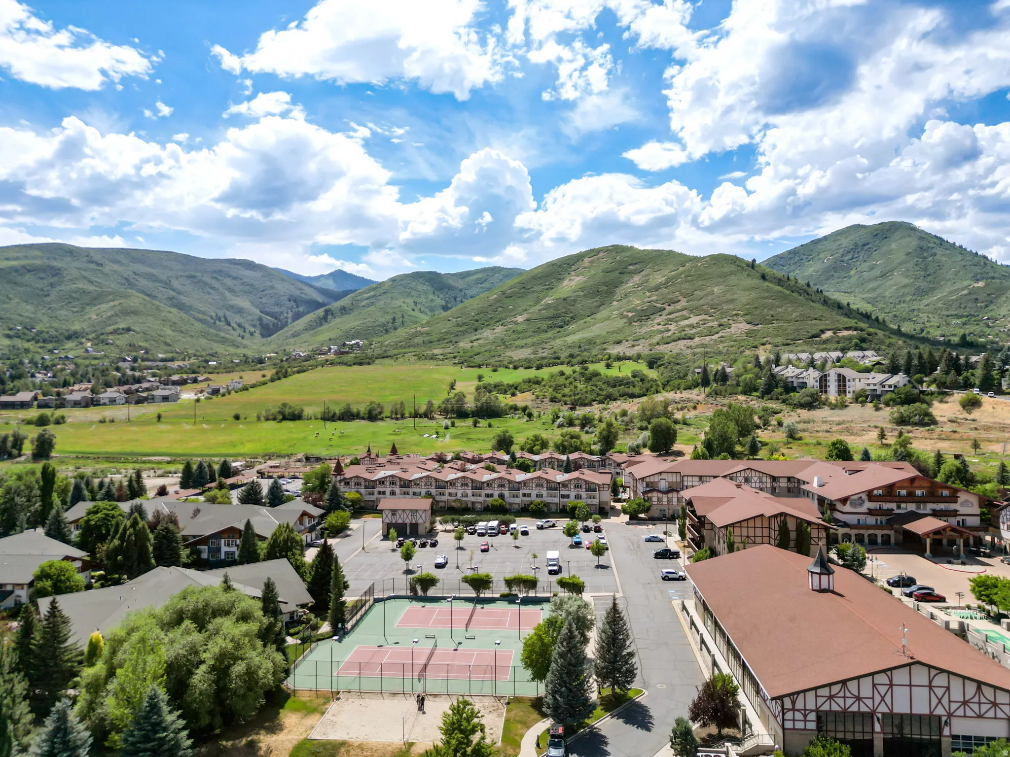 Alpine-style complex featuring multiple buildings, surface parking areas, and two tennis courts