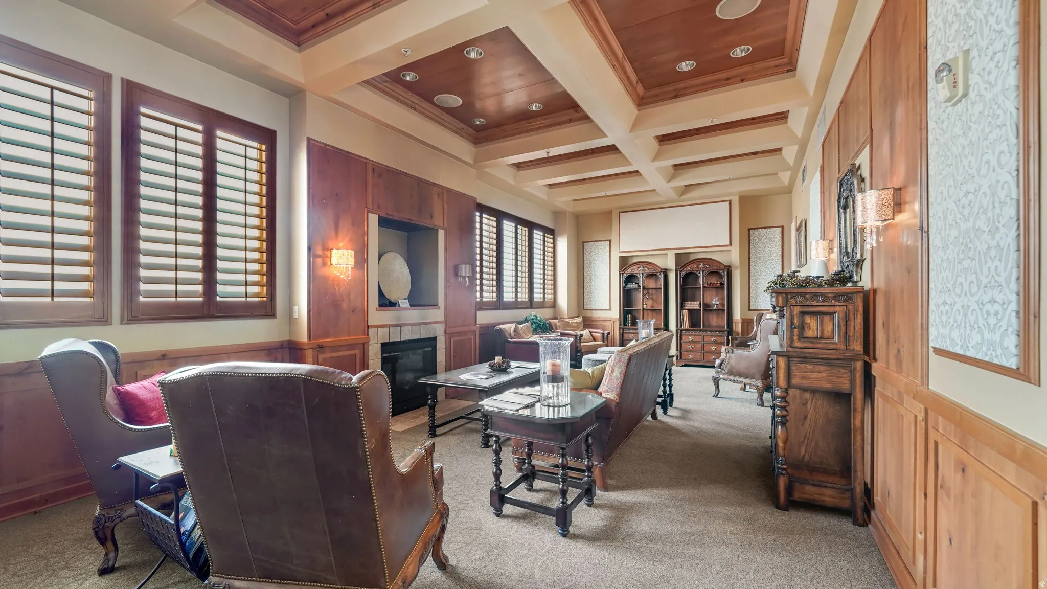 Spacious lounge featuring extensive wood paneling, a coffered ceiling with recessed lighting, and a built-in fireplace with a stone surround
