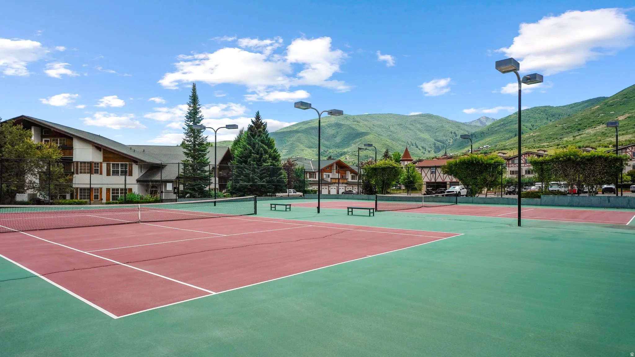 Tennis courts with hard surface flooring, surrounded by mature trees and mountain scenery