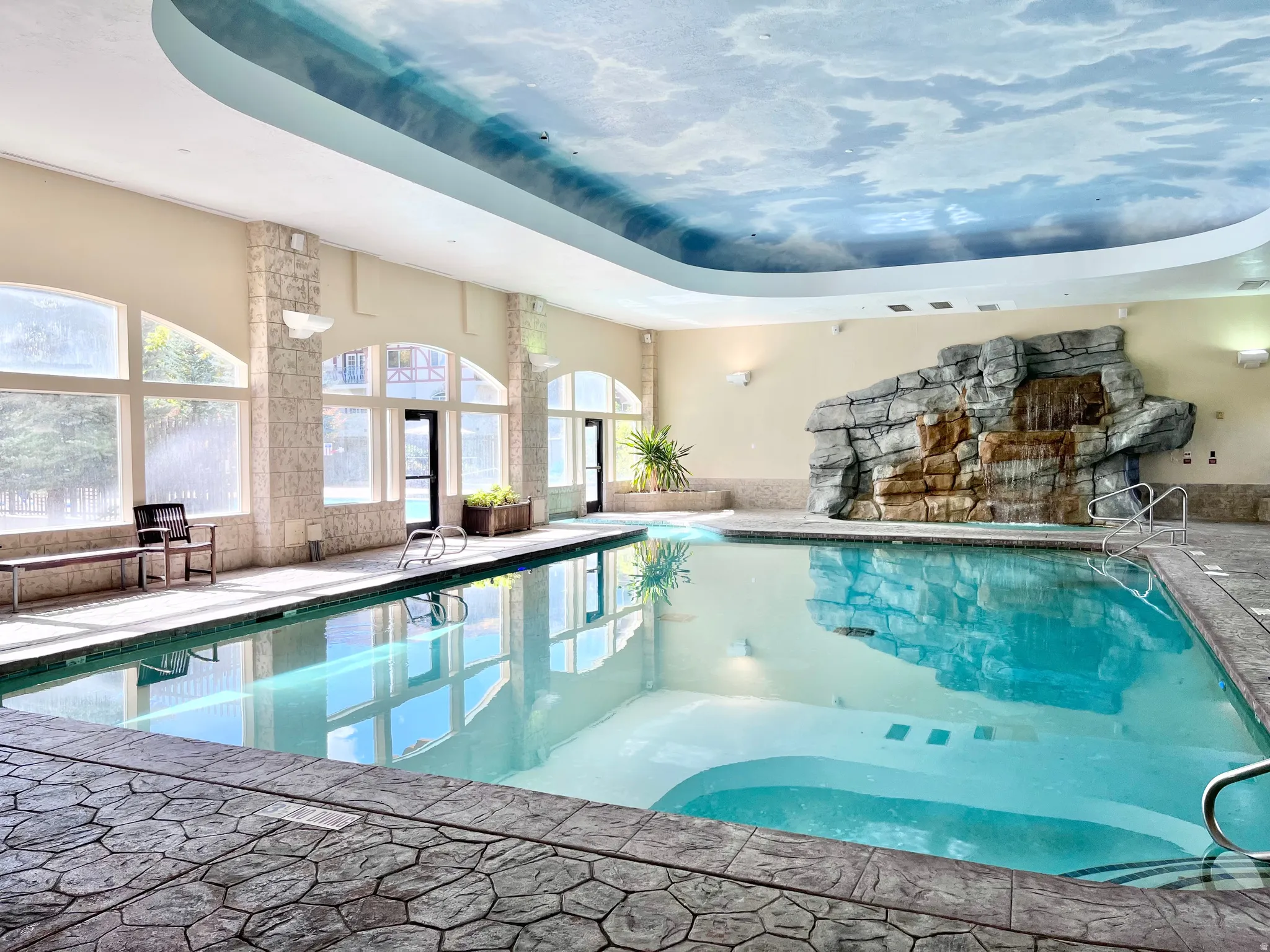 Indoor swimming pool featuring a waterfall rock formation and a custom cloud-mural ceiling