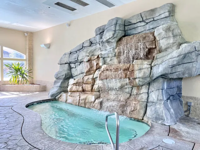Indoor spa featuring a rock waterfall, stamped concrete flooring, and an integrated planter with natural light from large windows