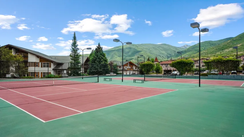 Tennis courts with hard surface flooring, surrounded by mature trees and mountain scenery