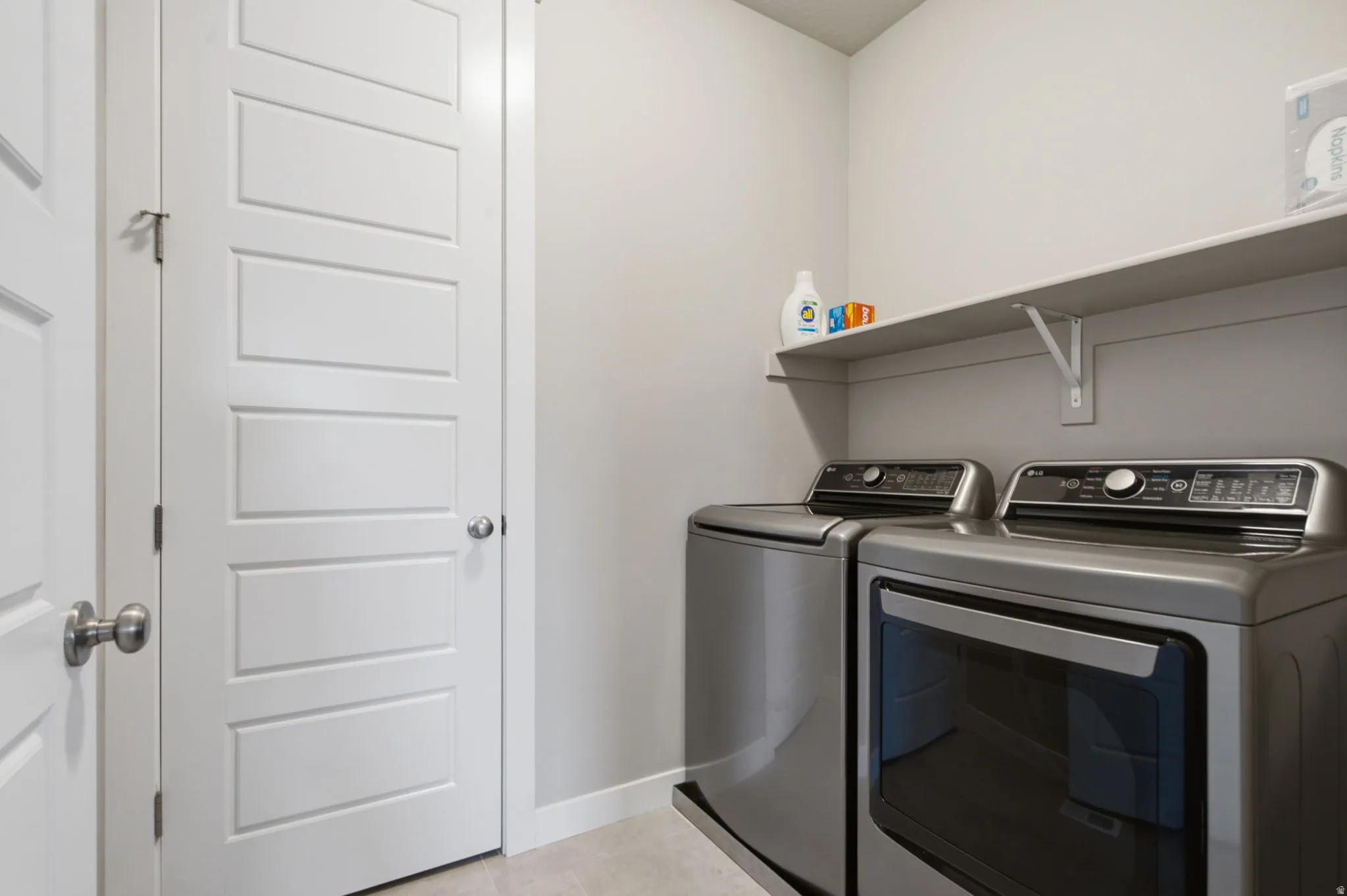 Dedicated laundry area featuring a wall-mounted shelving unit, light-toned wall paint, and white baseboards