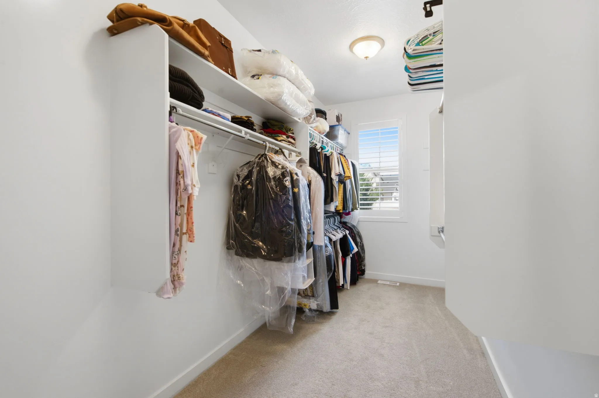 Walk-in closet featuring built-in shelving, hanging rods, an overhead light fixture, and a window with blinds