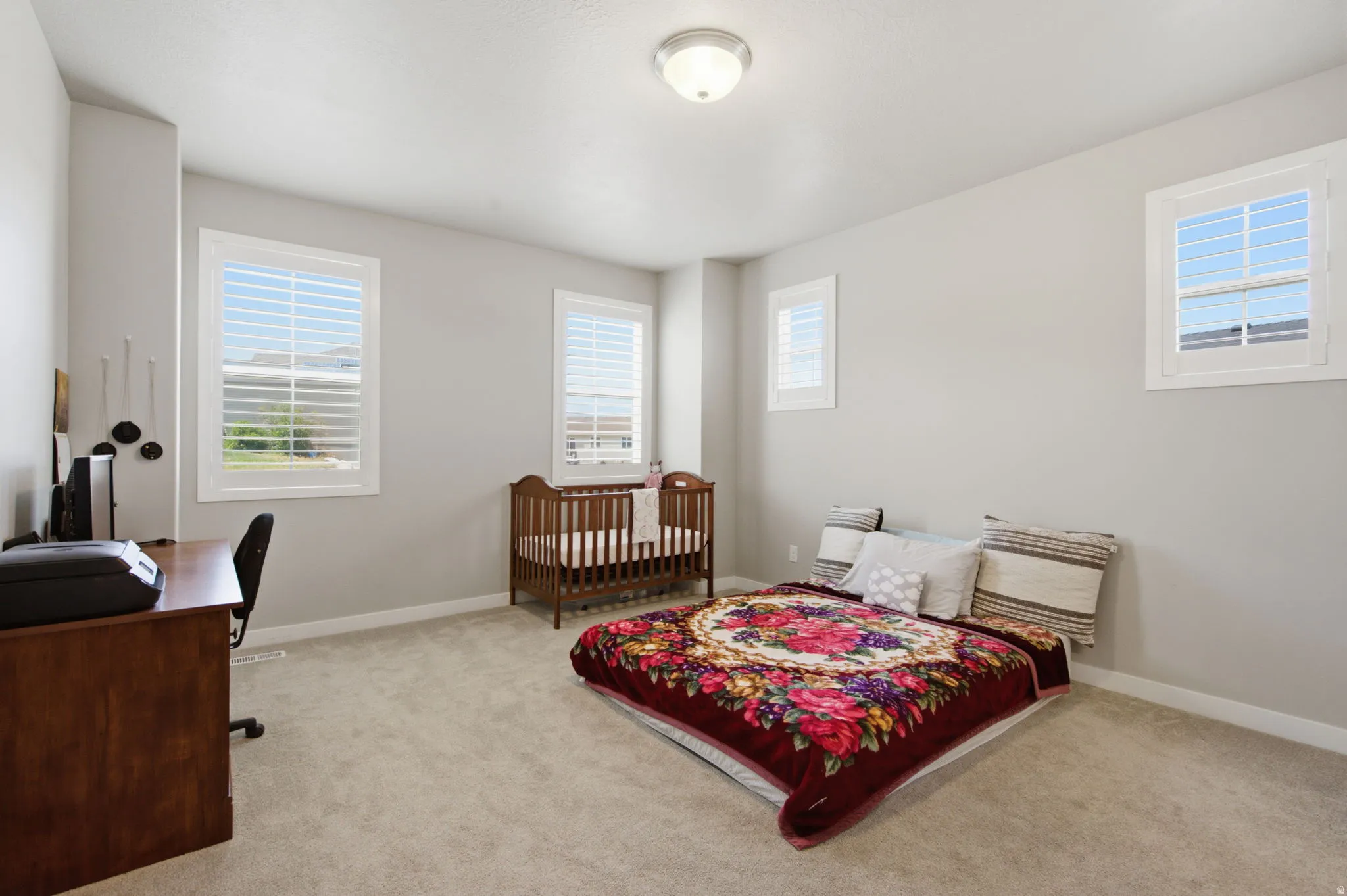 Carpeted room featuring multiple windows with white plantation shutters, neutral wall paint, and a ceiling-mounted light fixture