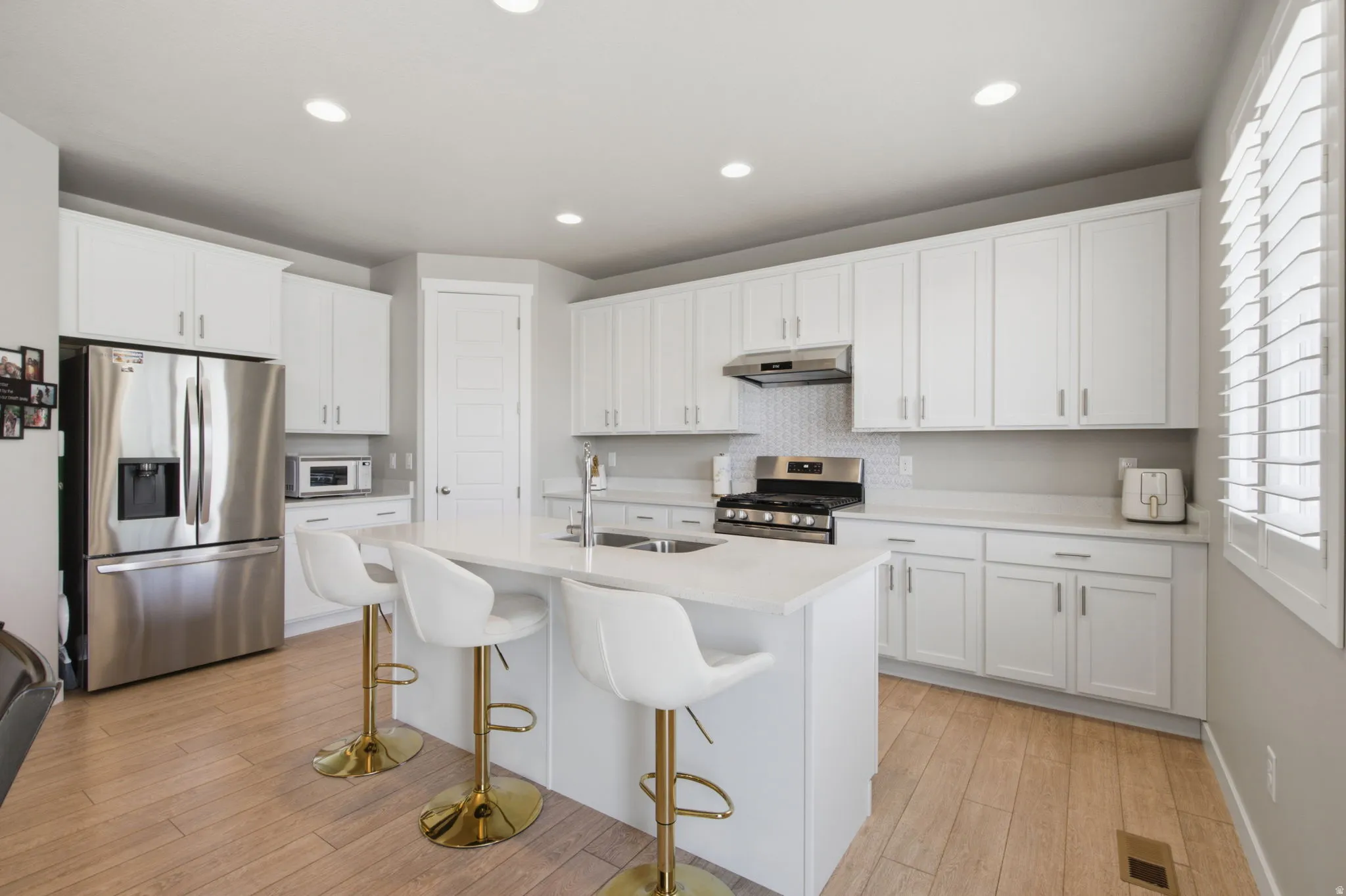 Spacious kitchen featuring an extended island, white shaker cabinetry, stainless steel appliances, a tile backsplash, and light wood-finish flooring
