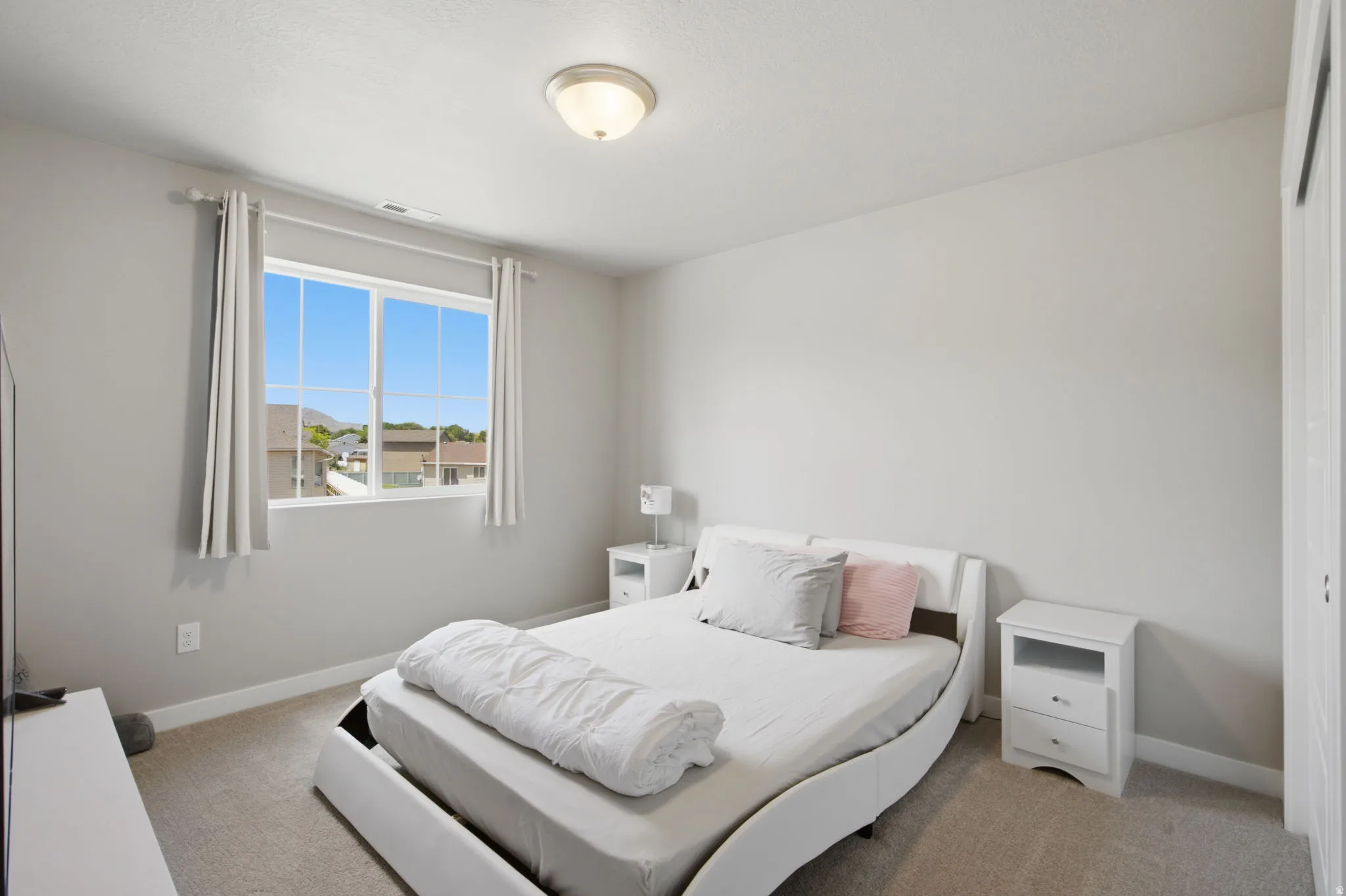 Carpeted bedroom featuring neutral wall tones, a large window with white framing, and a ceiling-mounted light fixture