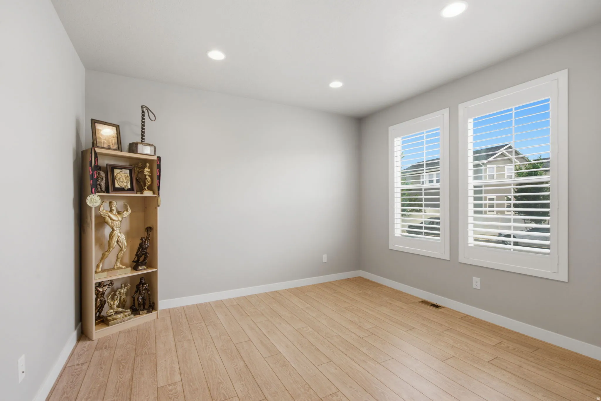 Room featuring light wood-finish flooring, two large windows with white louvered shutters, light gray wall paint, and recessed ceiling lighting