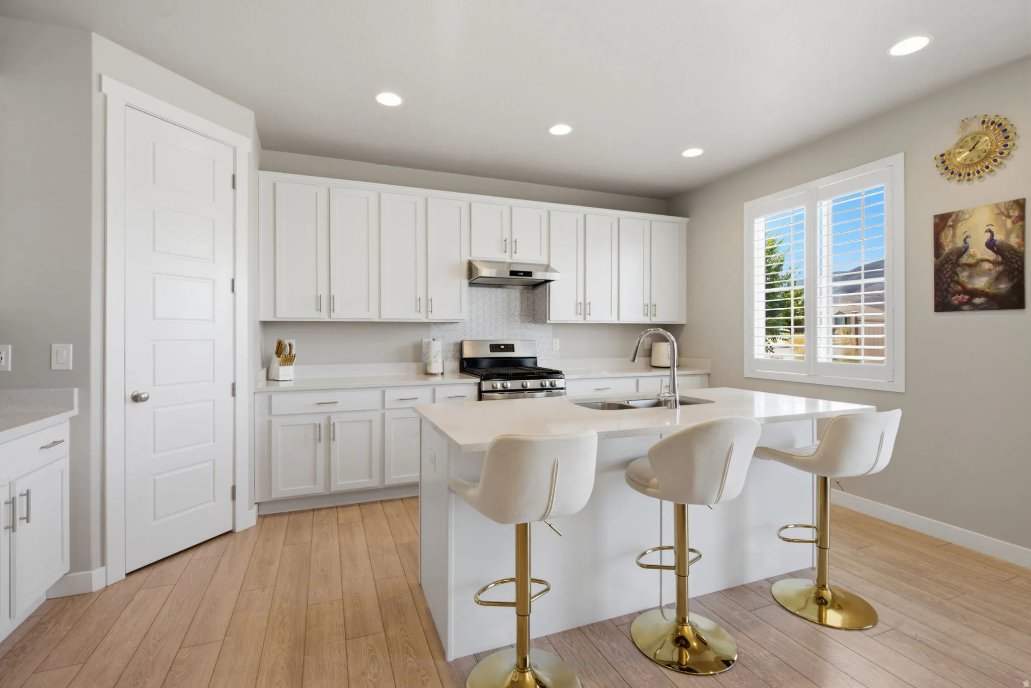 Modern kitchen featuring a central island with integrated sink, white cabinetry, stainless steel appliances, light wood-finish flooring, and recessed lighting