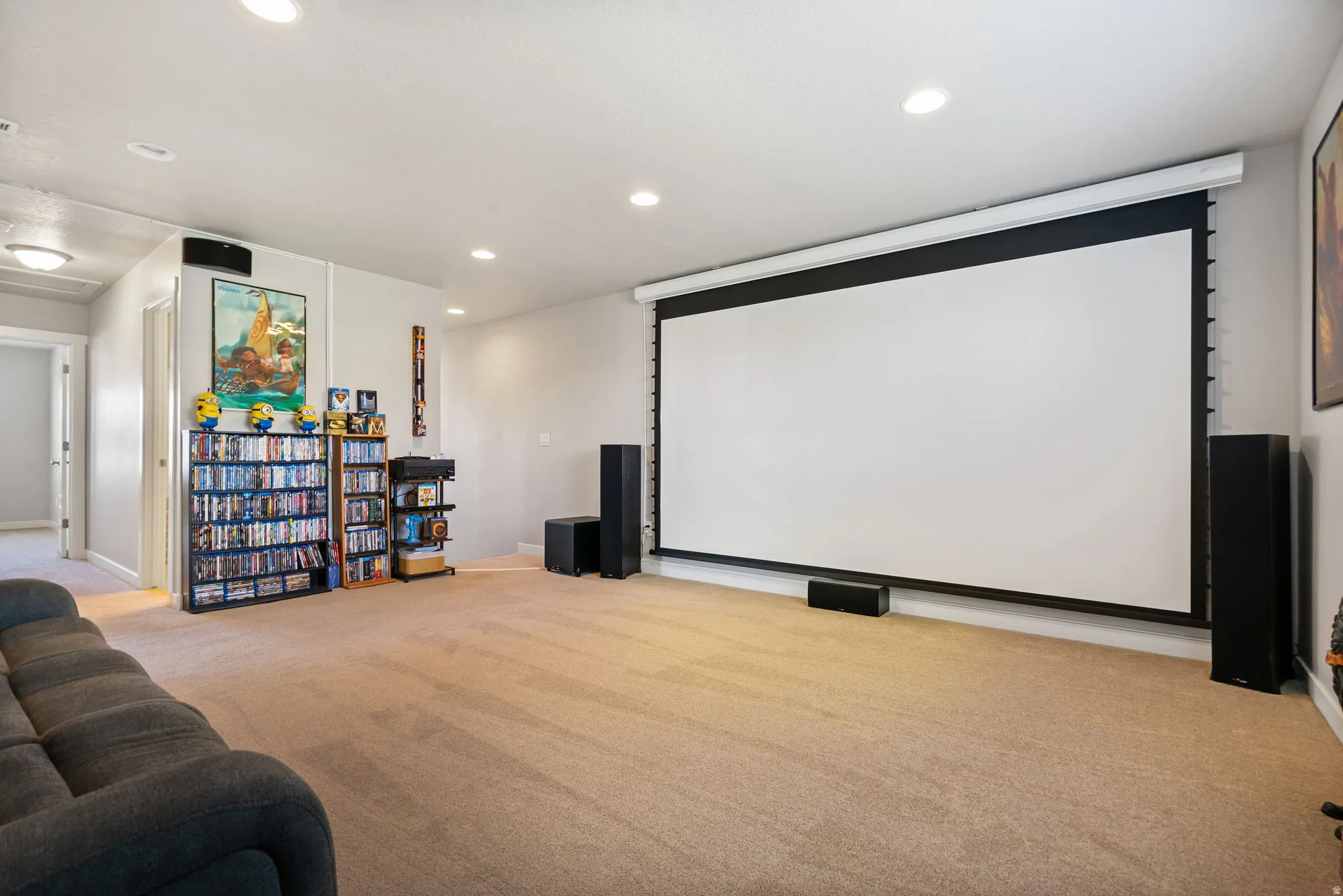Spacious entertainment room featuring a large retractable projection screen, neutral carpeting, and recessed lighting