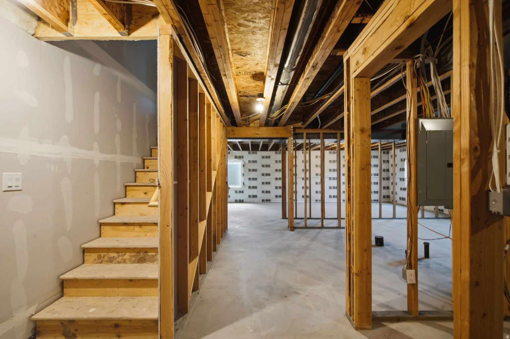 Unfinished basement featuring exposed wood framing, concrete flooring, and an electrical panel
