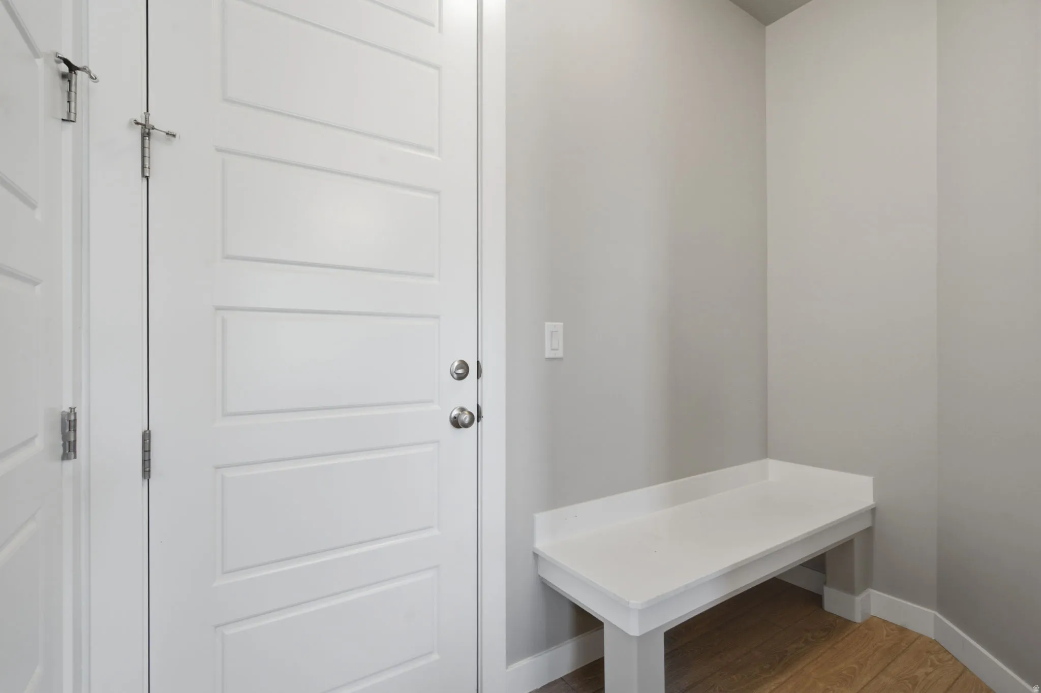 Entryway featuring a built-in bench, light gray wall color, wood-finish flooring, and a paneled door with polished chrome hardware