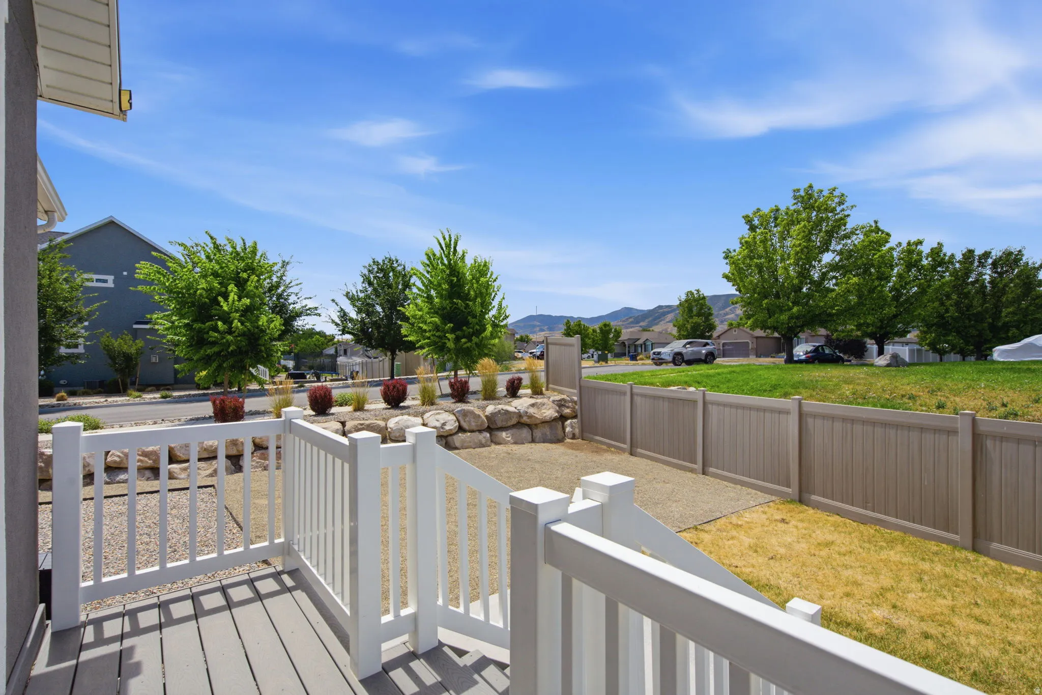 Deck with white railings and gray composite decking, featuring a gravel side yard and a light brown privacy fence