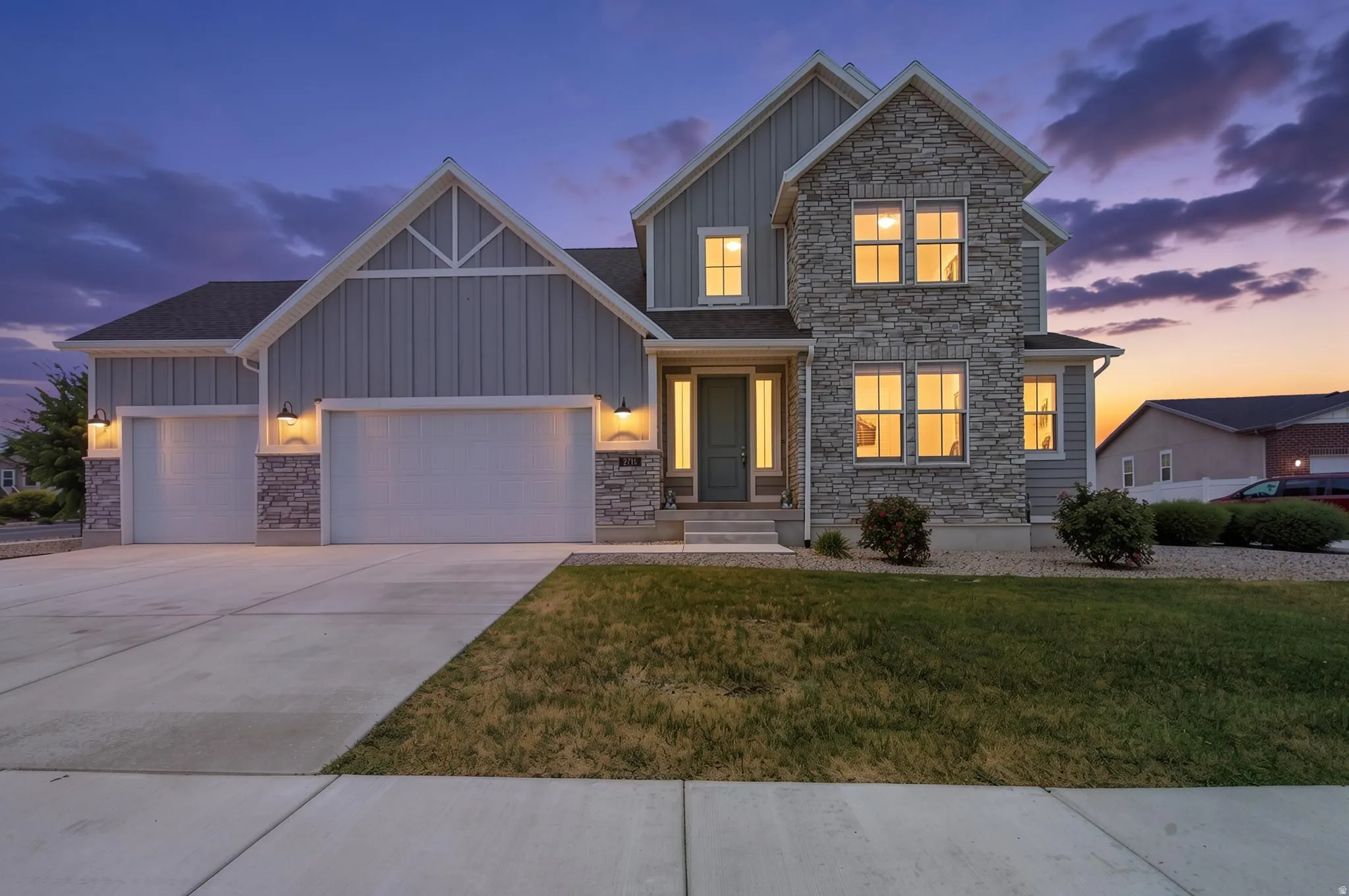 Modern farmhouse exterior featuring board and batten siding, stone veneer accents, a prominent two-car garage, and a light gray front door with sidelights