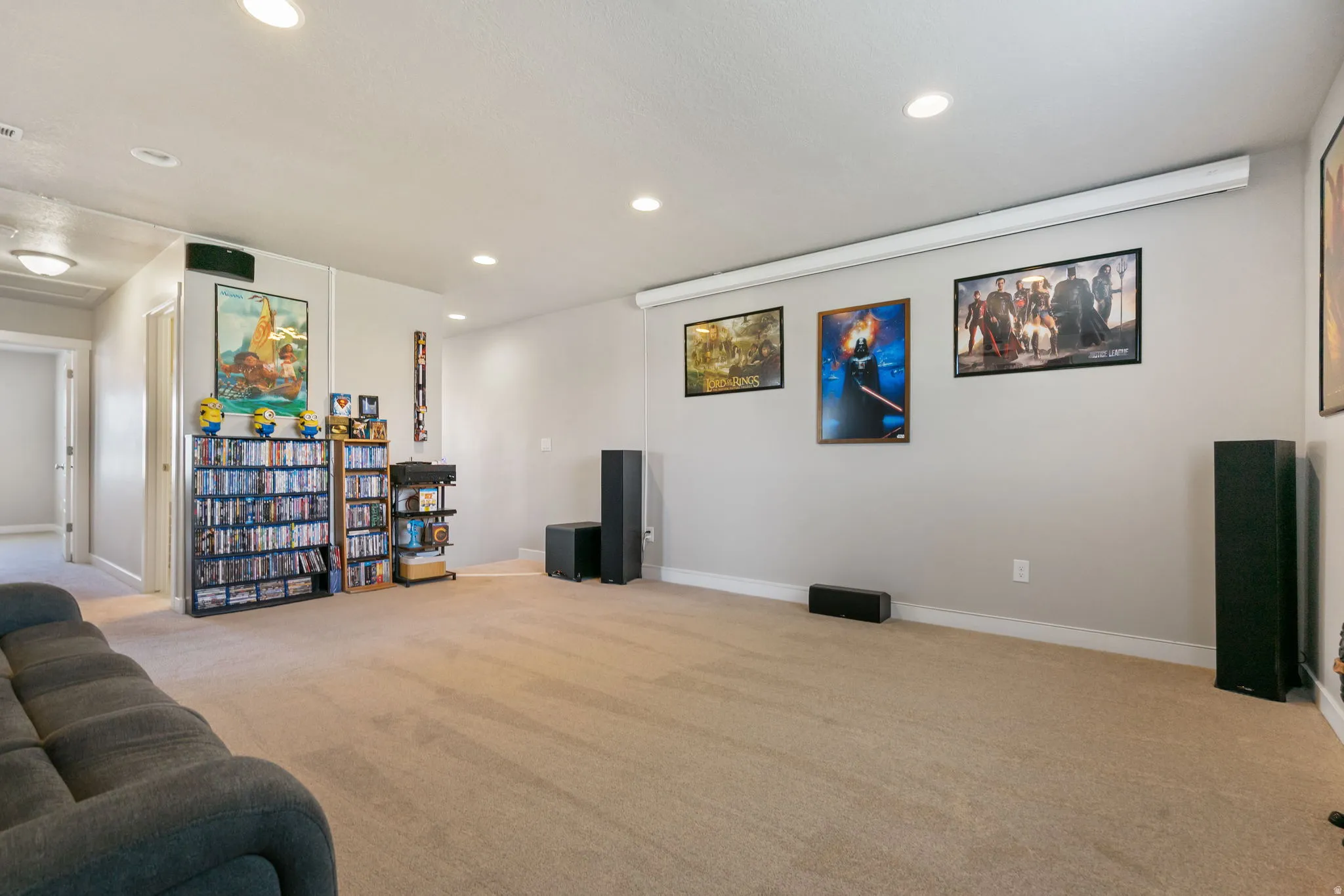 Spacious room featuring neutral carpeting, recessed ceiling lighting, and a wall-mounted projection screen