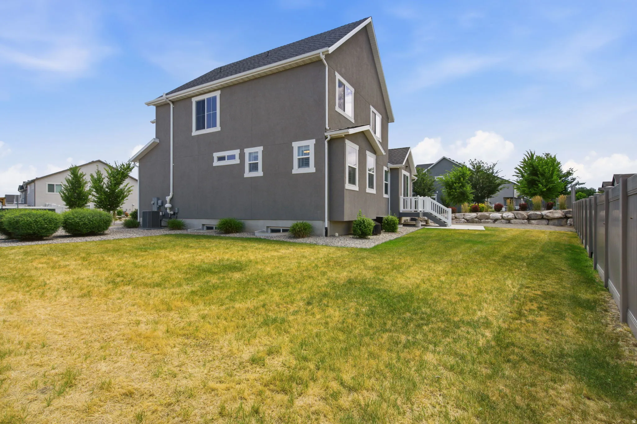 Spacious rear yard with a neutral-toned privacy fence, mature landscaping, and a multi-level deck with white railings