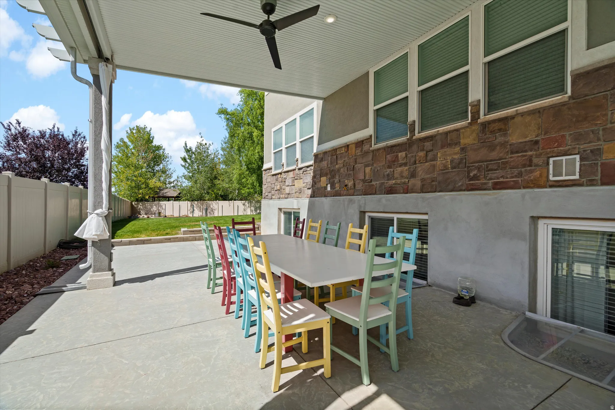 Covered patio featuring a ceiling fan, concrete flooring, and a stone-clad exterior wall