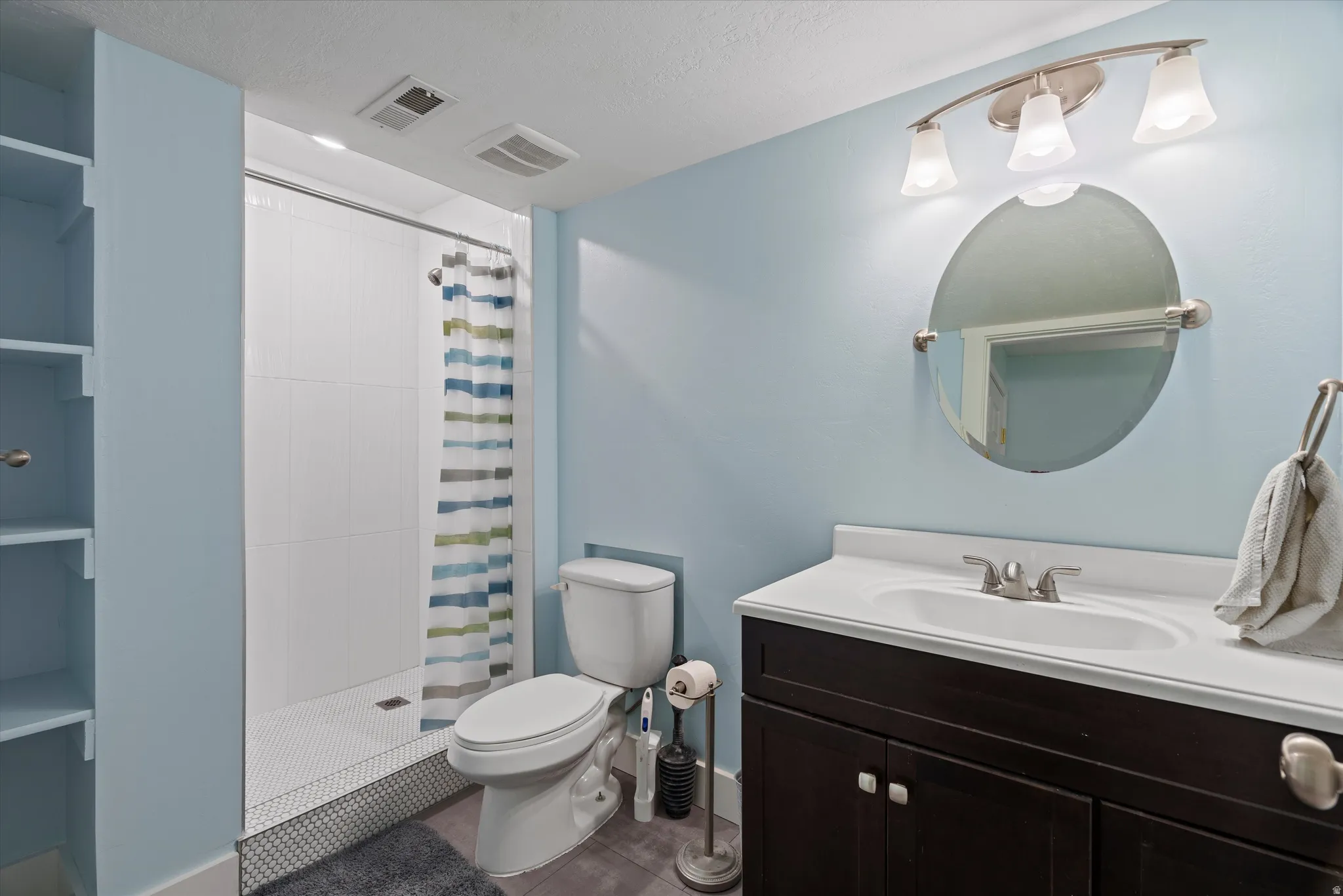 Bathroom featuring a single vanity with dark wood cabinetry, an integrated sink, and a circular mirror